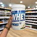 Close-up of (PER4M Whey Protein Powder 900g) held up inside My Supplement Shop, clearly showing the front label in a Sports Nutrition setting.