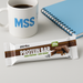 PER4M Protein Bar on a modern desk with MSS mug and blue notebook – Desk Snack lifestyle image for MySupplementShop ecommerce listing.